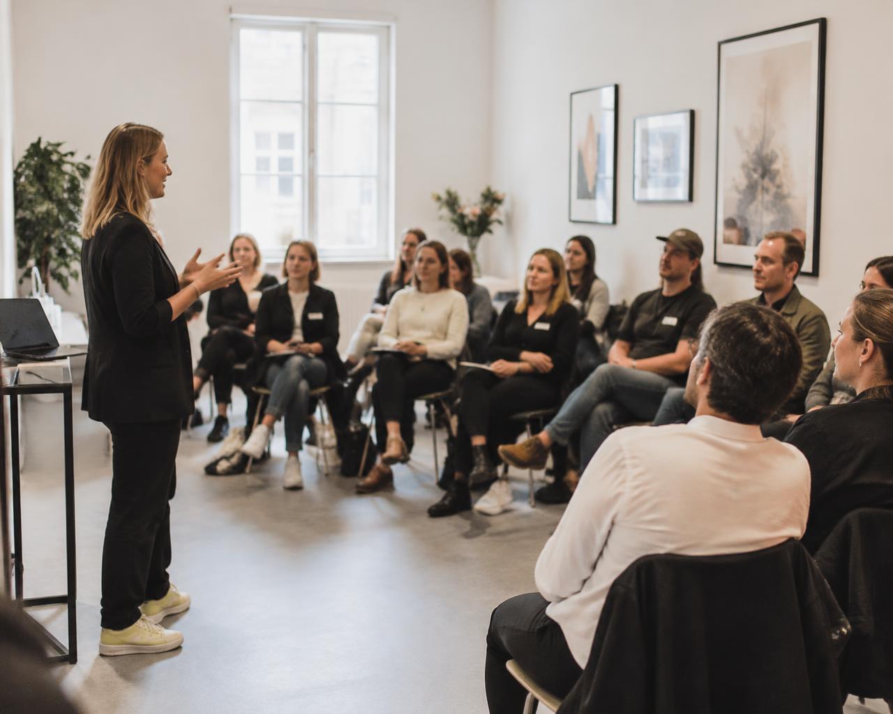Előadó beszél egy kisebb workshop résztvevőinek világos teremben